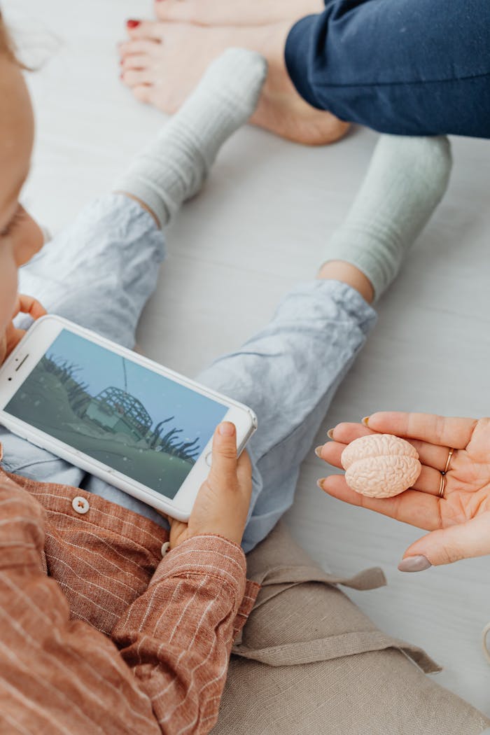 Child playing an educational game on a smartphone while holding a brain model.